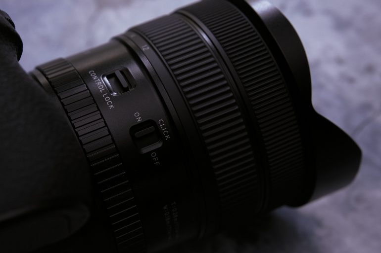 Close-up of a black camera lens with control lock and click on/off switches visible.