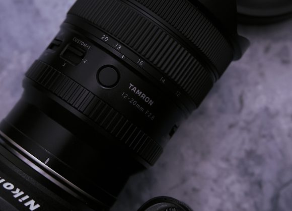 Tamron 12-20mm F2.8 Review: The Amazing Light and Nimble Astro Photography Lens Close-up of a Tamron 12-20mm F2.8 camera lens attached to a Nikon camera on a gray surface.