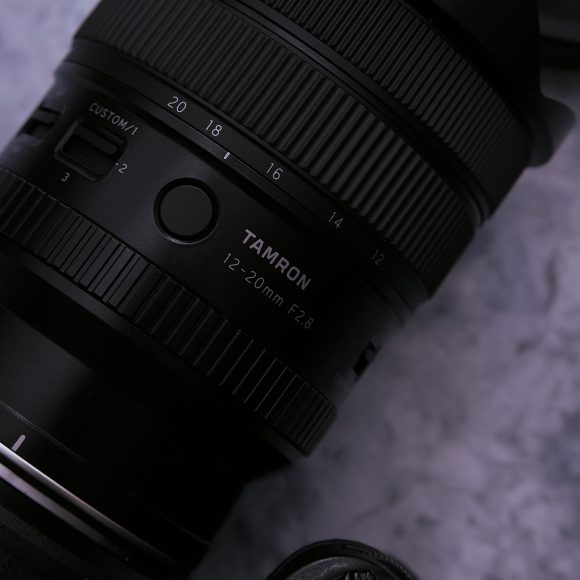 Close-up of a Tamron 12-20mm F2.8 camera lens attached to a Nikon camera on a gray surface.