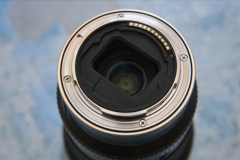 A close-up of the back side of a camera lens showing its metal mount and electronic contacts.