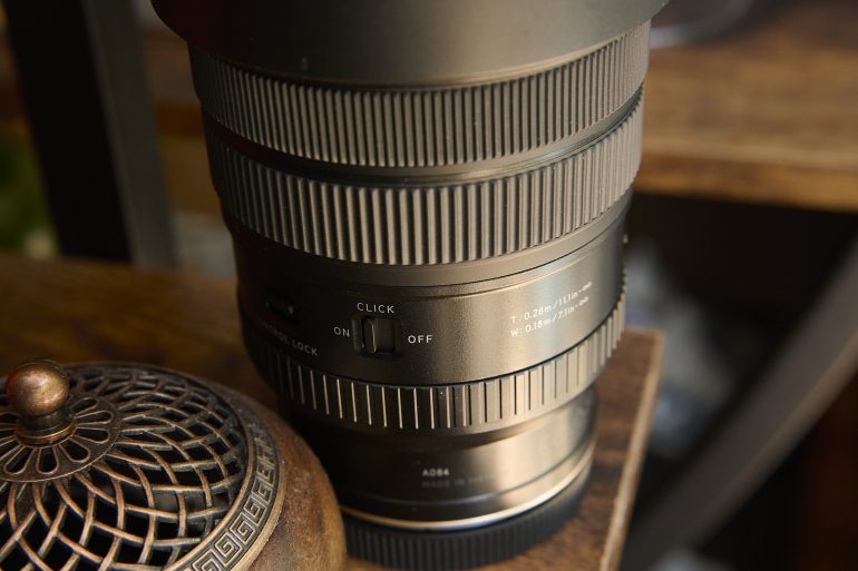 Close-up of a camera lens with adjustment switches, sitting next to a decorative metal object on a wooden surface.