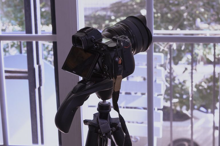 Camera on a tripod facing a bright window with trees and cars visible outside.