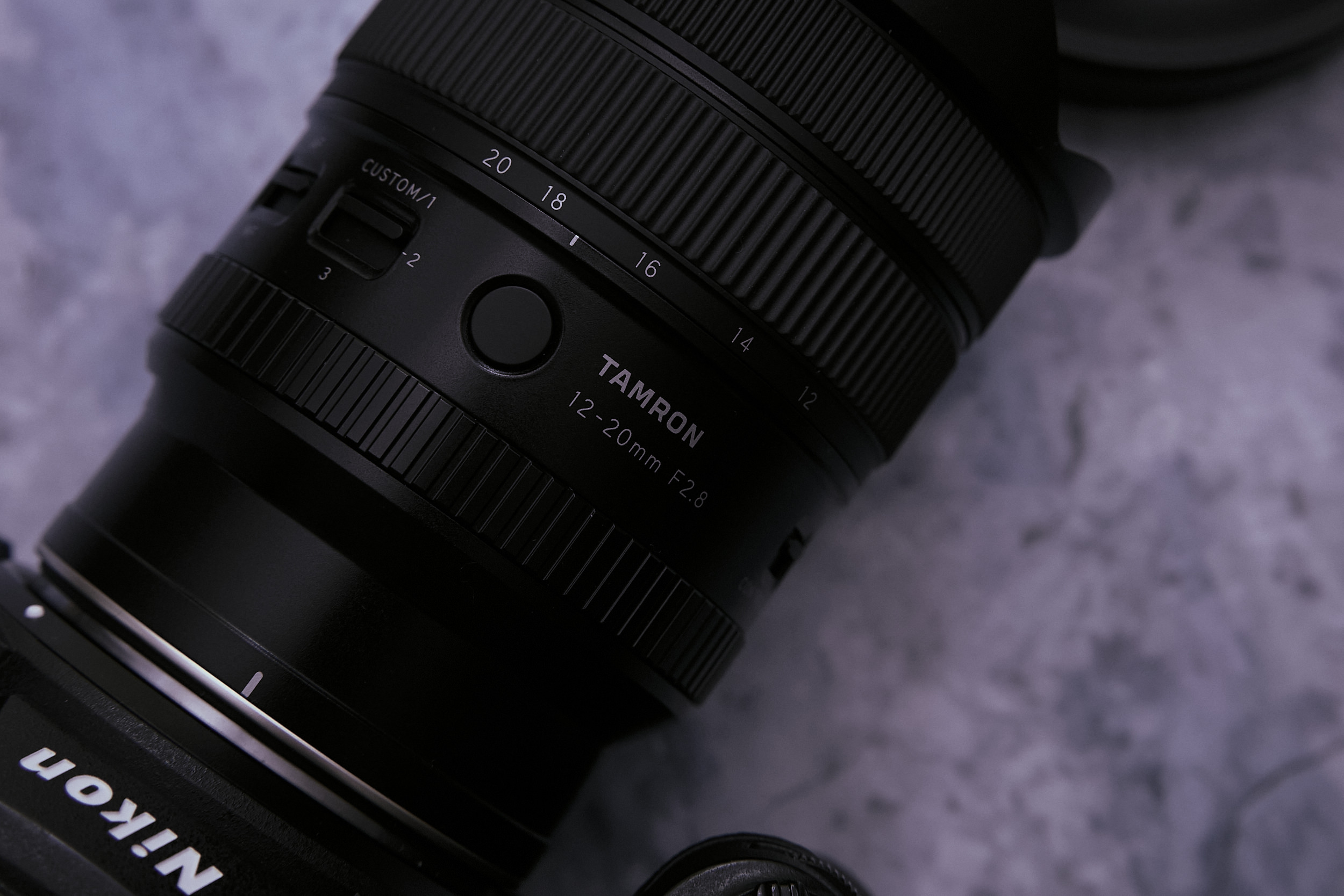 Tamron 12-20mm F2.8 Review: The Amazing Light and Nimble Astro Photography Lens Close-up of a Tamron 12-20mm F2.8 camera lens attached to a Nikon camera on a gray surface.