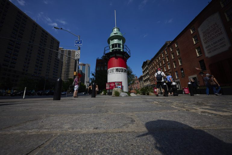 Low-angle view of the red and white lightship museum with people walking by on a sunny day.