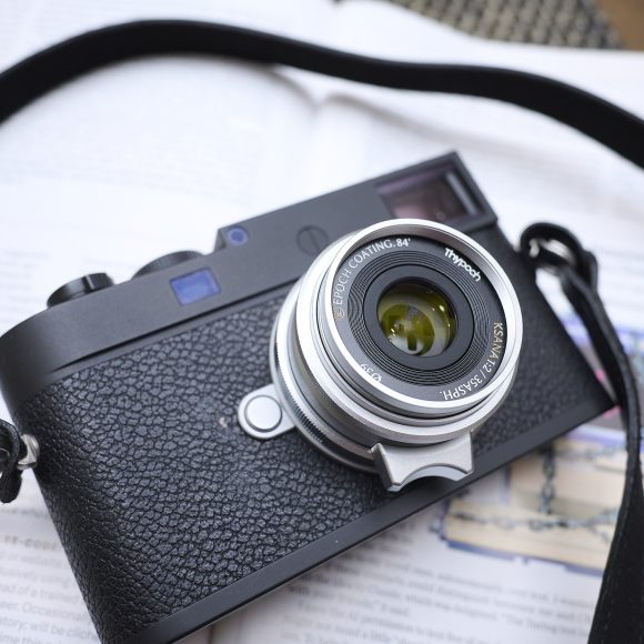 A black camera with a lens and strap rests on an open book with blurred text and images.