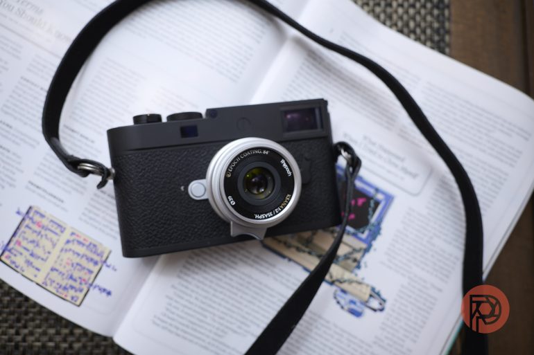 A black camera with a strap rests on an open magazine with printed text and a red circular logo.