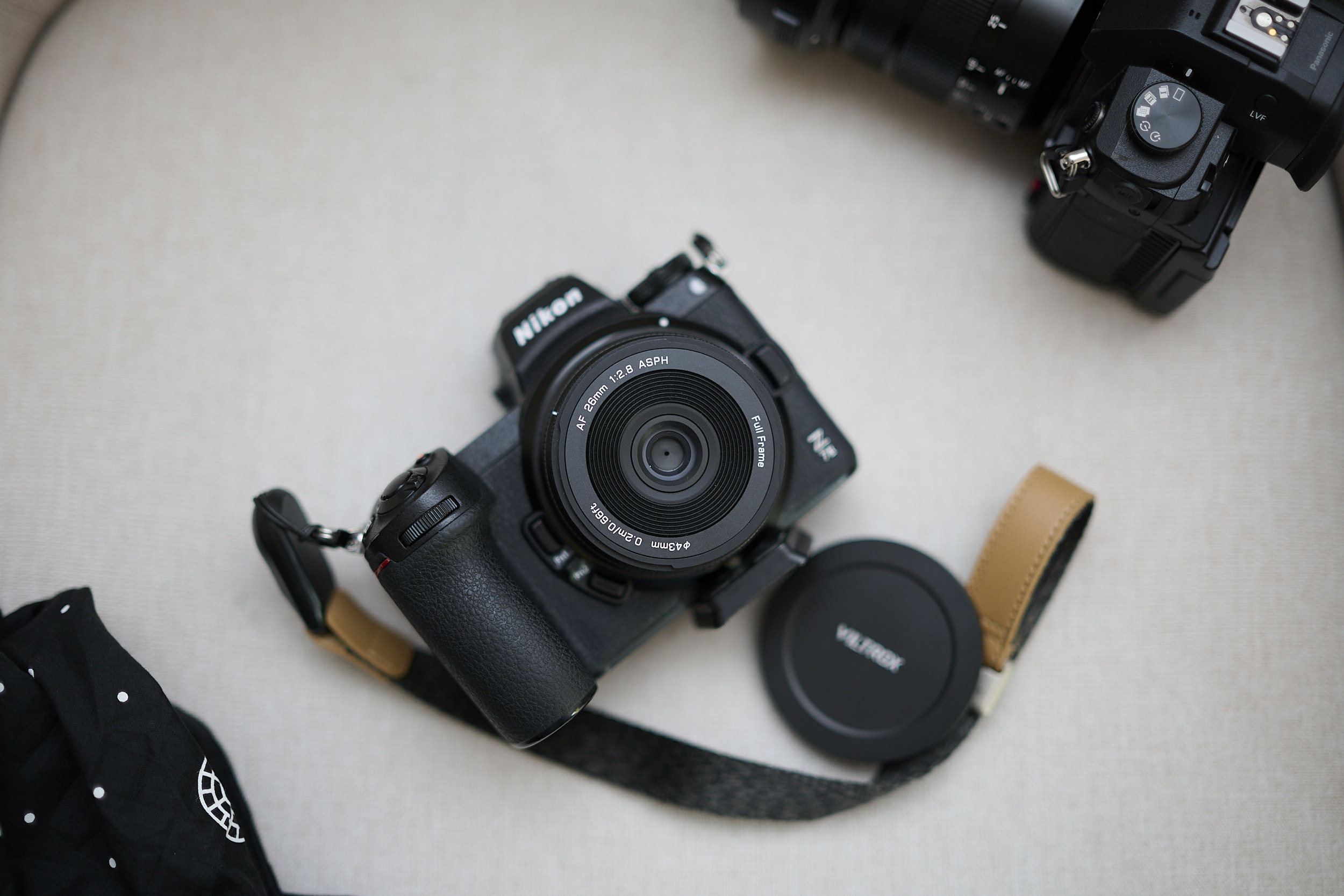 Viltrox 26mm F2.8 EVO Review: It Turned My Nikon Z7 II Into an EDC Camera A Nikon camera with lens and strap, lens cap removed, sits on a light surface beside another camera.