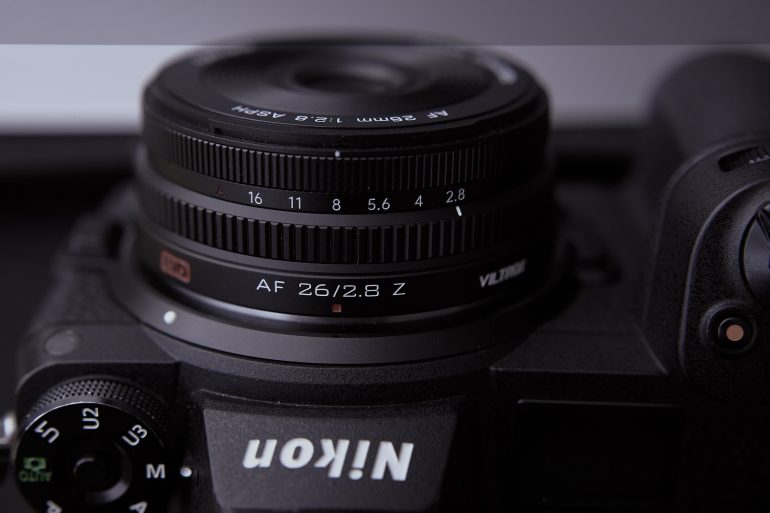 Close-up of a Nikon camera with a 26mm f/2.8 Z lens, showing lens markings and camera controls.