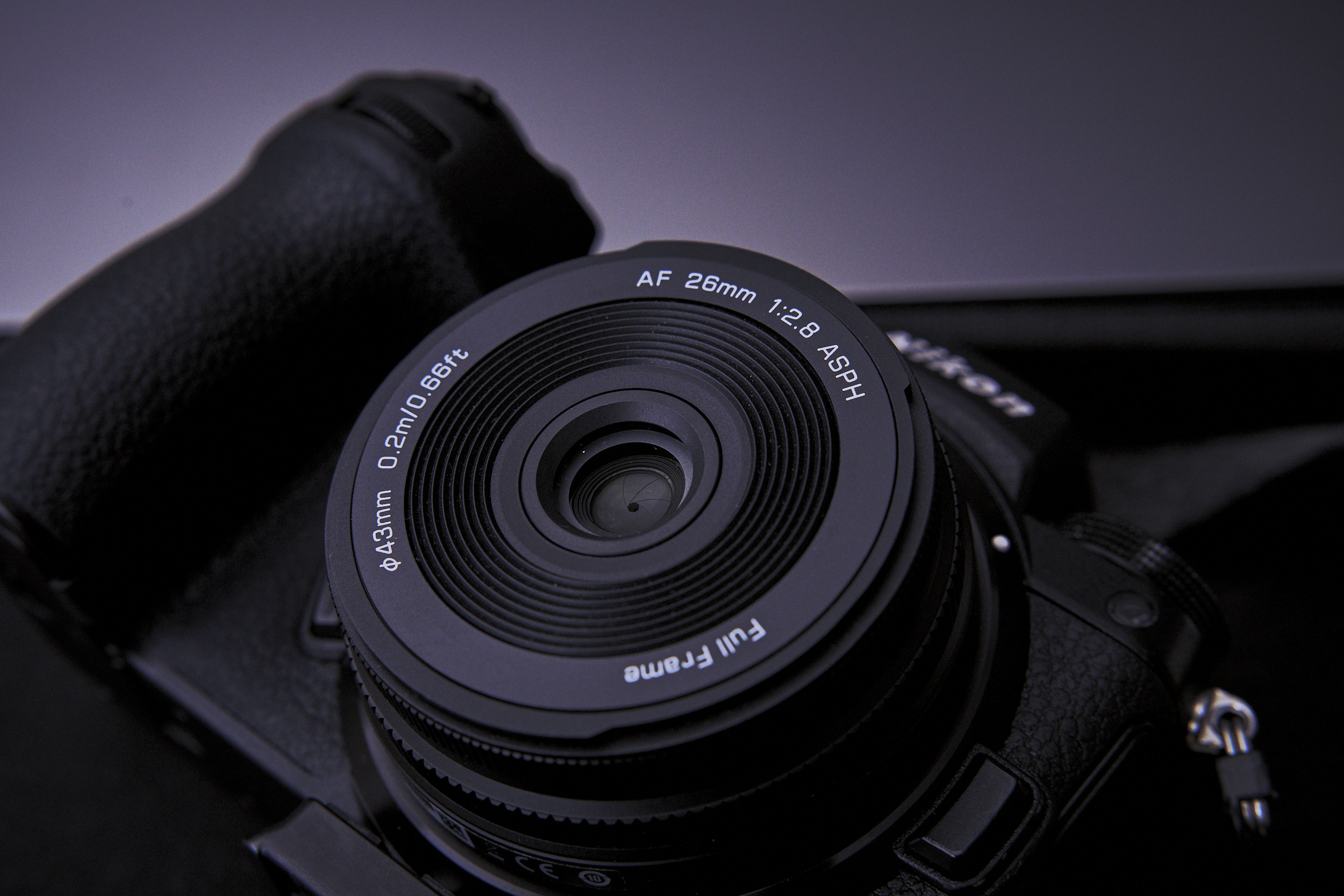 Close-up of a black digital camera with a 26mm f/2.8 ASPH lens against a dark background.