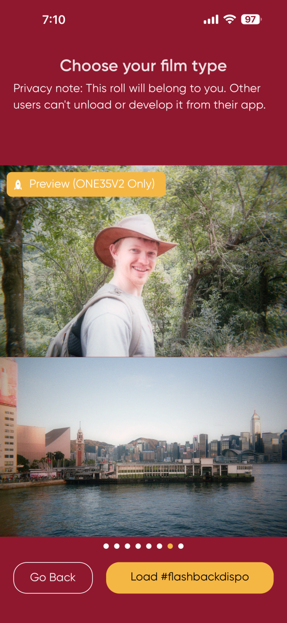 A smiling person in a hat outdoors above a cityscape with water, buildings, and skyline under a blue sky.