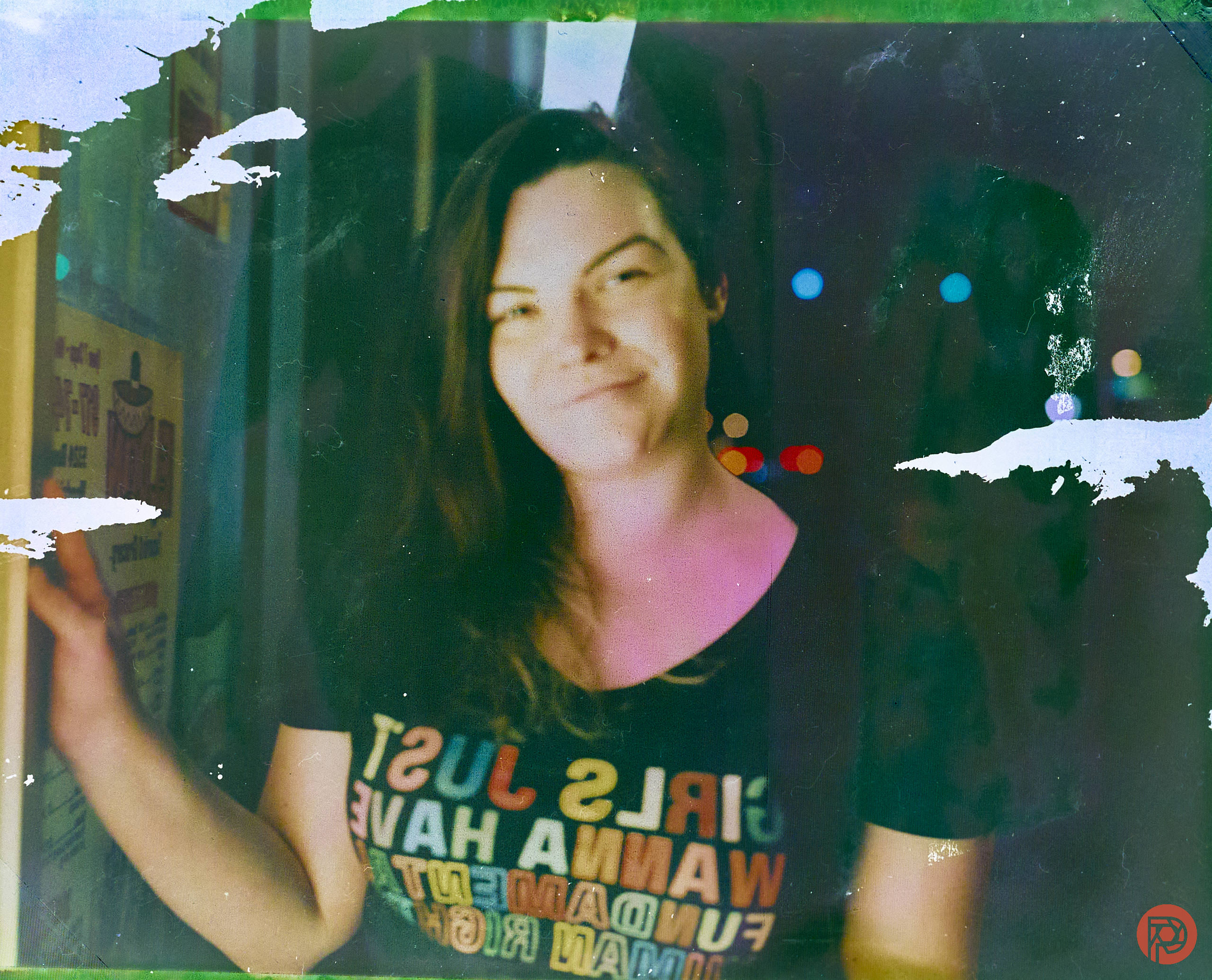 Smiling person with long hair wears a GIRLS JUST WANNA HAVE FUNDAMENTAL HUMAN RIGHTS shirt at night.