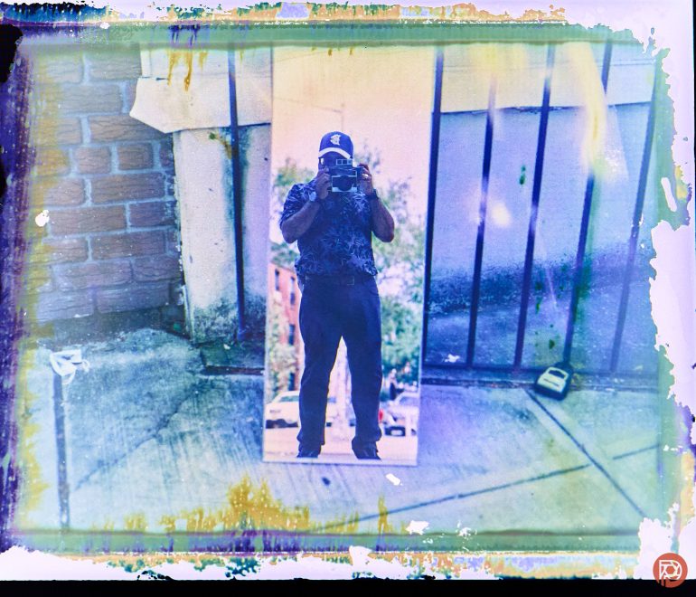 A person takes a photo in a mirror outdoors, with colorful, distressed edges framing the image.