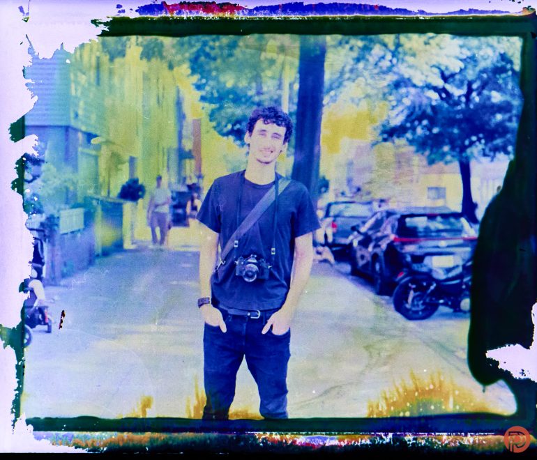 Man stands on a city street with a camera around his neck, surrounded by vibrant, colorful light effects.