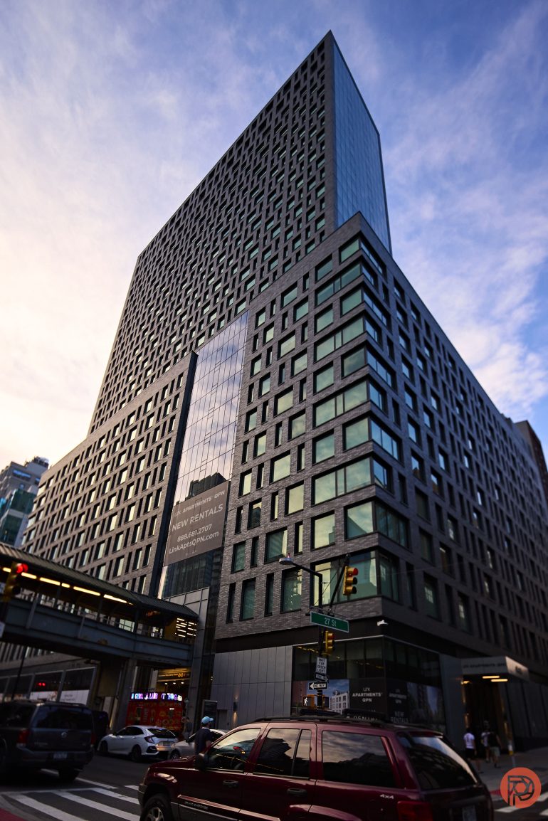 A modern high-rise building with large glass windows at a city intersection during sunset.