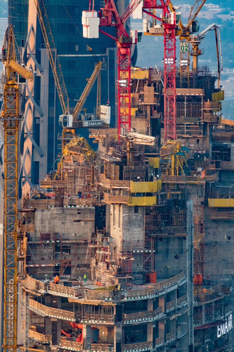 A close-up of a high-rise building under construction with cranes and workers on multiple floors.