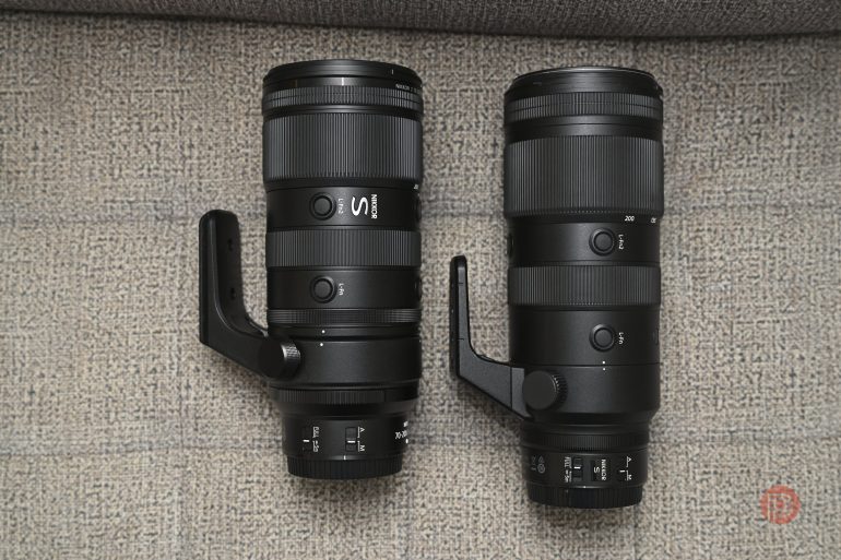 Two black camera lenses with tripod mounts placed side by side on a textured light gray surface.