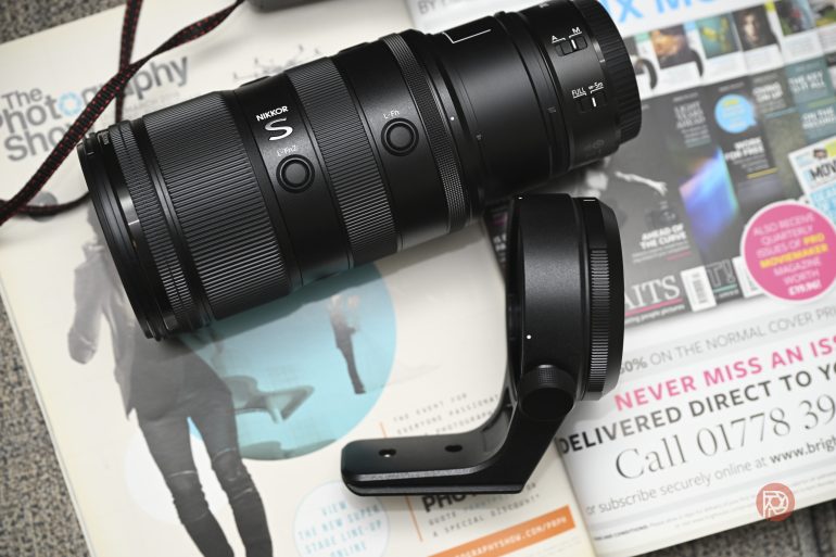 A Nikon S camera lens and tripod mount rest on photography magazines and brochures.