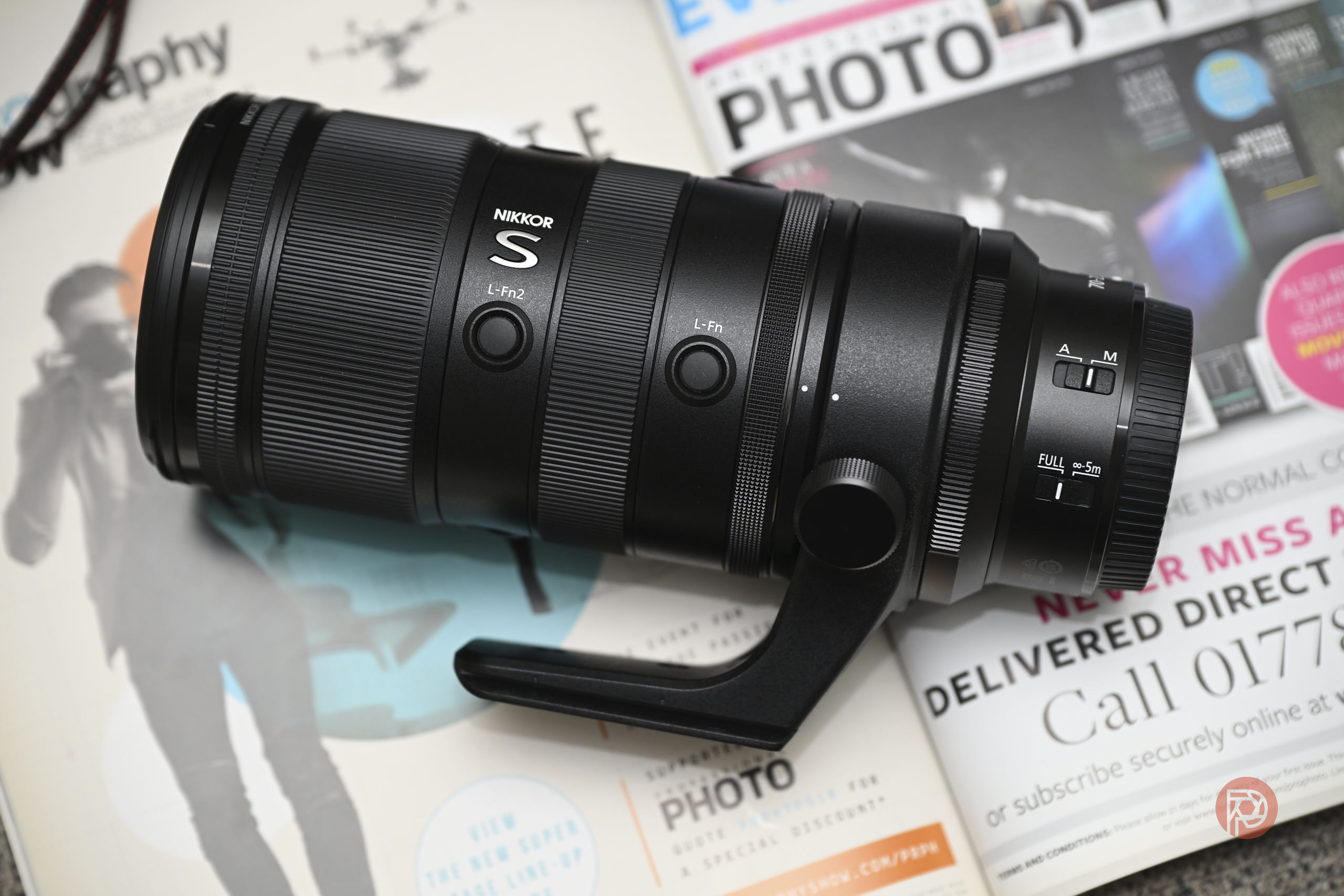 Nikon Z 70-200mm f2.8 S VR II Review Update: Awesome For Sports Photography A Nikon NIKKOR S camera lens resting on top of several open photography magazines.