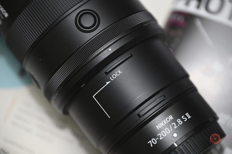 Close-up of a Nikkor 70-200mm f/2.8 S II camera lens showing the lock switch and lens details.
