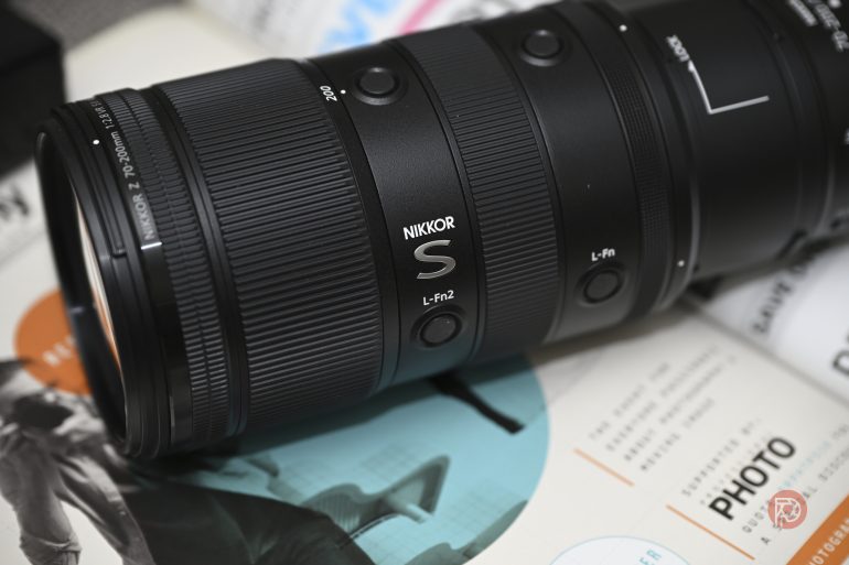 Close-up of a Nikon NIKKOR S camera lens resting on a magazine with photos and text.