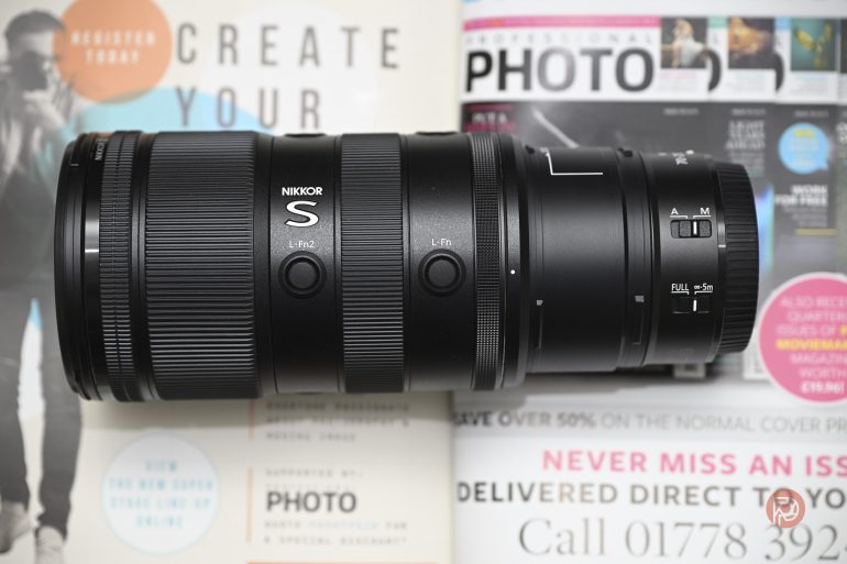 A Nikon NIKKOR camera lens lies on top of colorful photography magazines.