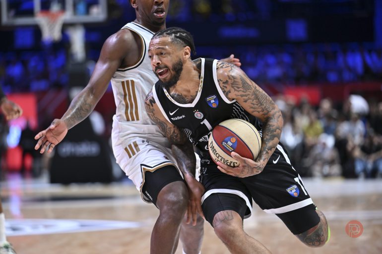 A basketball player in a black jersey drives past a defender on an indoor court during a game.
