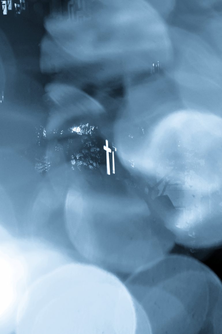 A glowing cross in the center, surrounded by blurred blue and white lights, creating an ethereal effect.