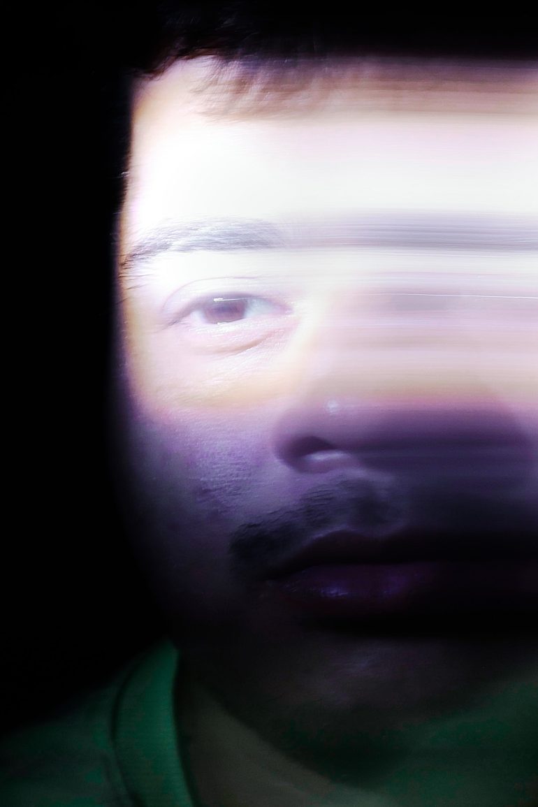 A mans face in low light, partially blurred with horizontal motion, creating a distorted effect.