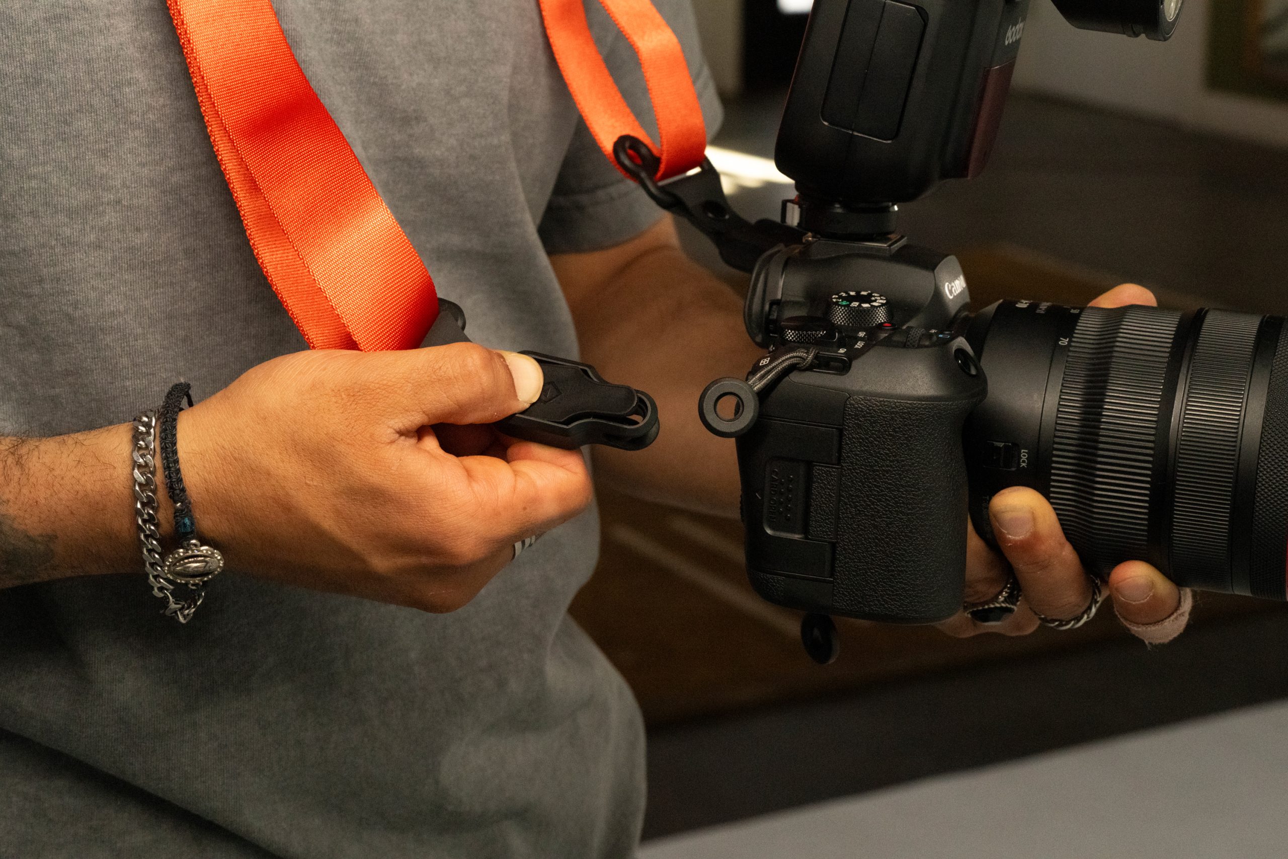 WANDRD Just Announced the Camera Strap of the Future on Kickstarter Person attaching an orange camera strap to a DSLR camera, wearing bracelets and rings.