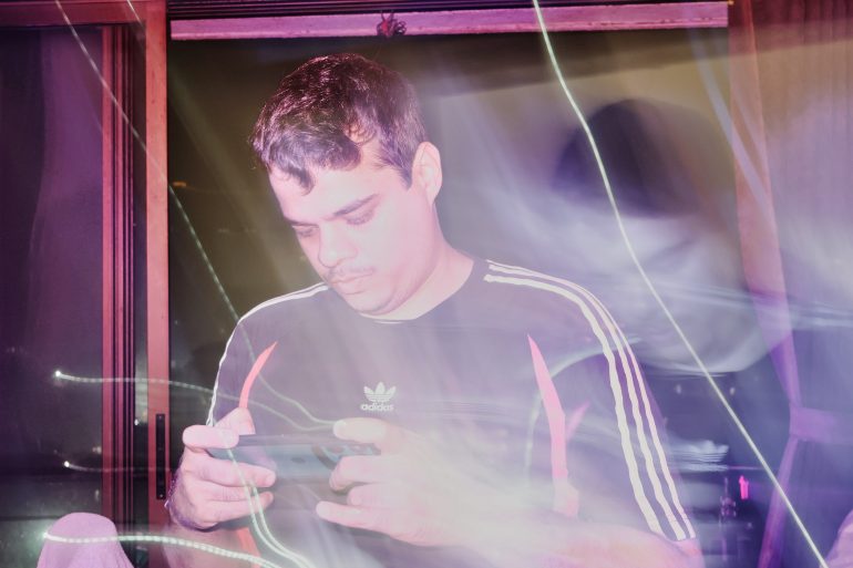Man in Adidas shirt using a smartphone, with bright light streaks and a hazy, colorful effect around him.