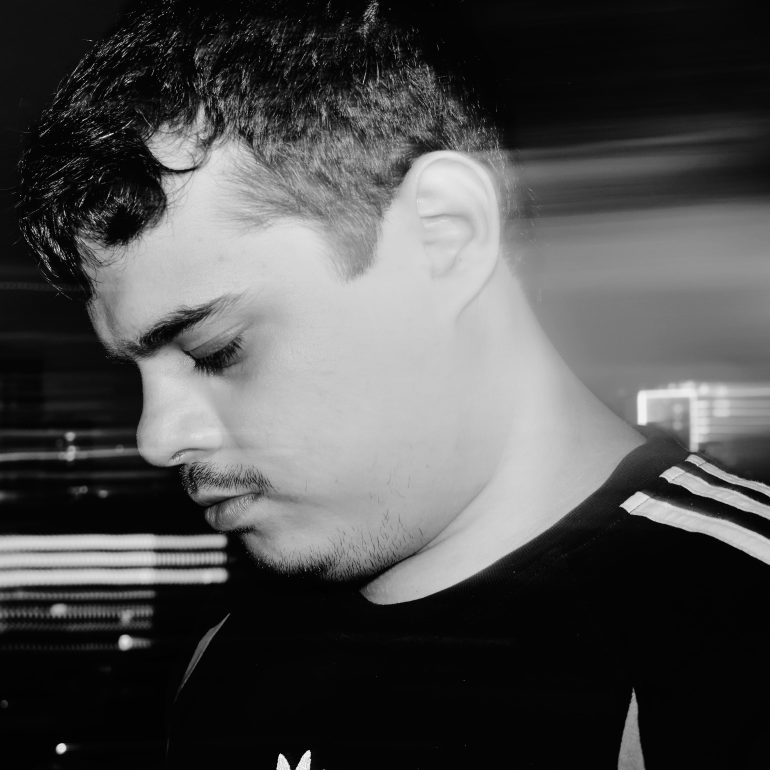 Man with short hair looking down, in black and white, with blurred light streaks in the background.