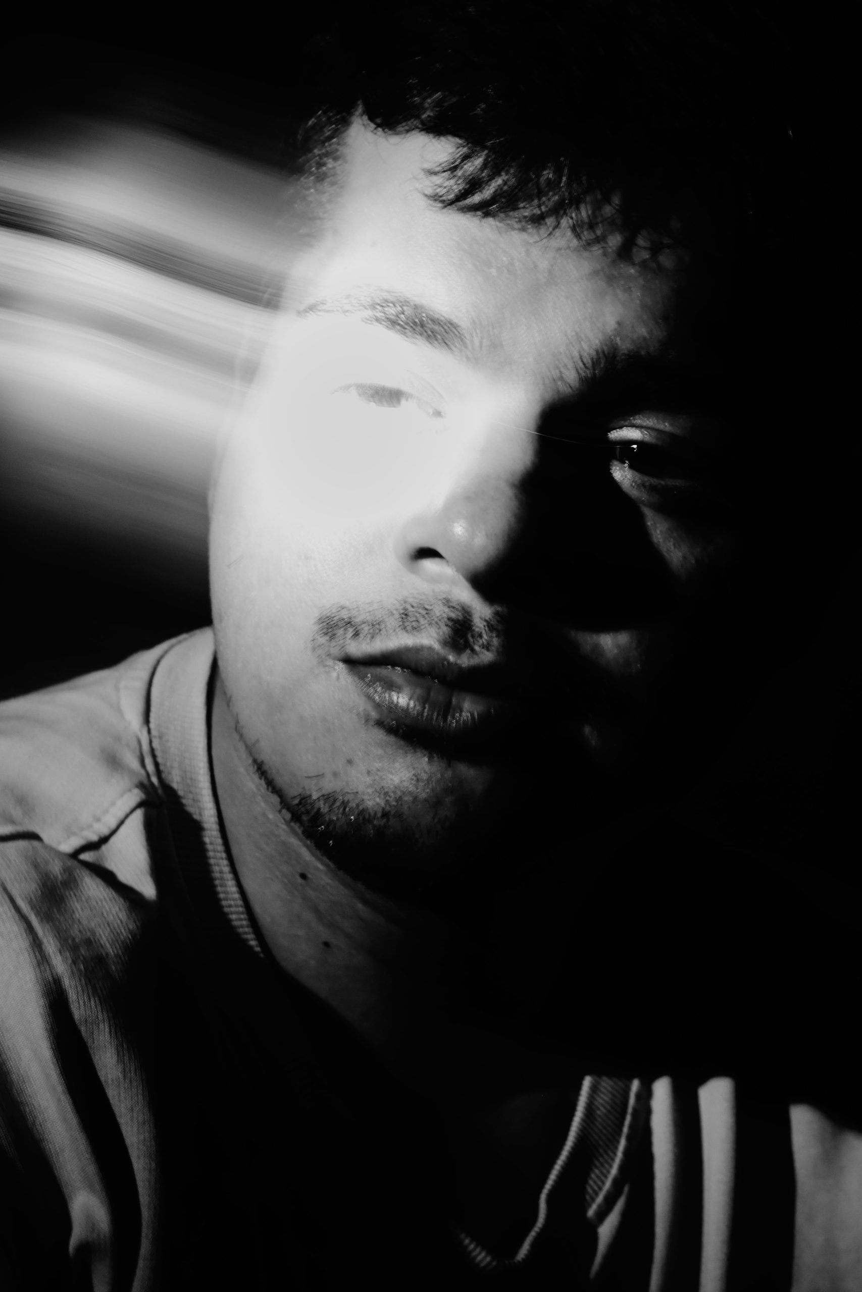 Try This: The Camera Trick for the Bored Photographer Black and white photo of a mans face partially lit with a bright streak of light across his eyes.