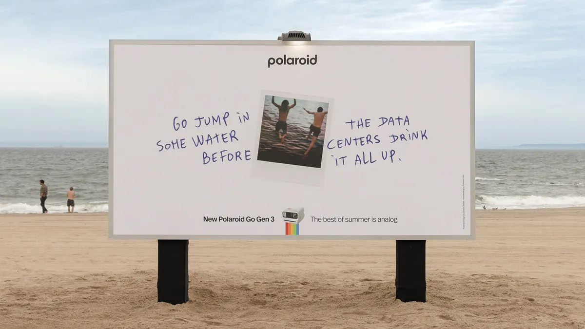 Billboard on a beach with a Polaroid photo and handwritten text about jumping in the water before data centers drink it up.