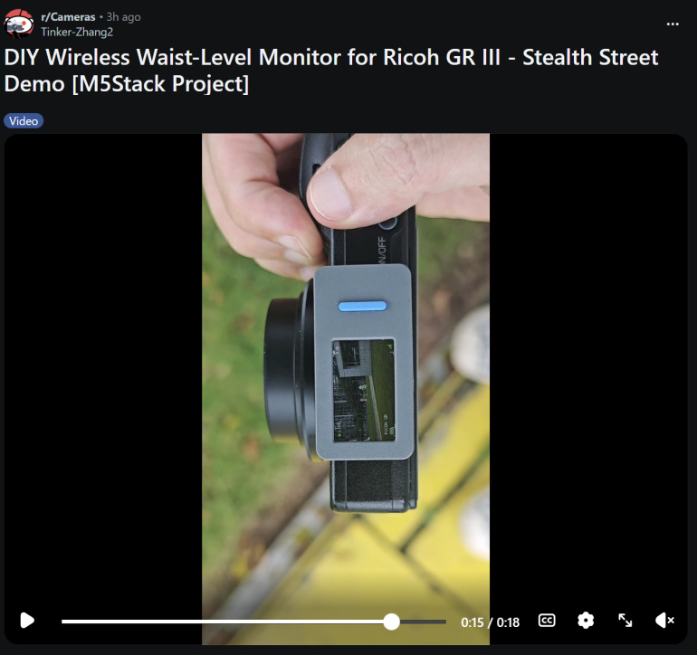 Close-up of a hand holding a Ricoh GR III camera with a small wireless monitor attached, outdoors.