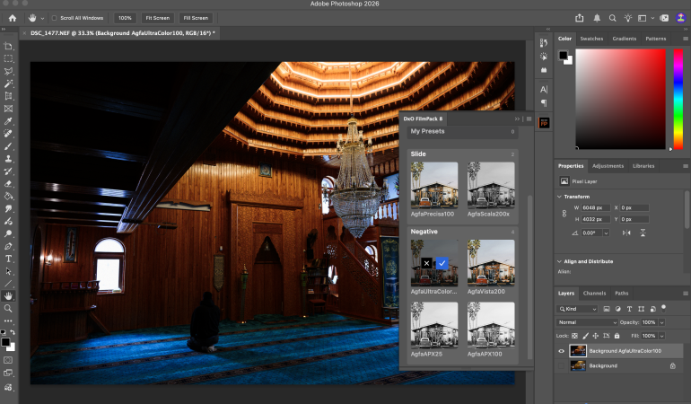 A person sits on a blue carpet in a wood-paneled mosque, editing the photo in Adobe Photoshop.