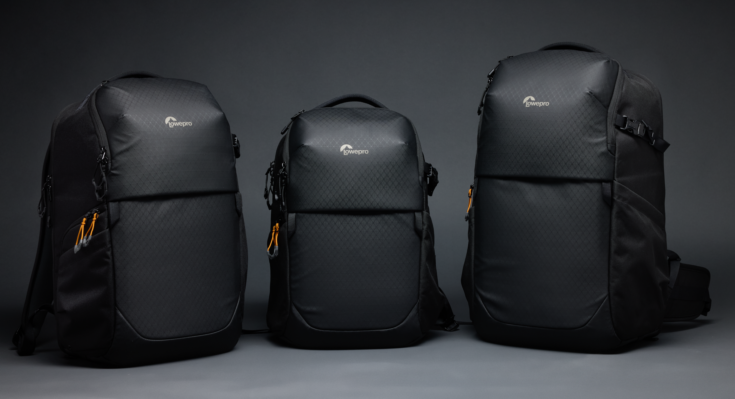 Three black camera backpacks of different sizes are displayed side by side on a dark background.