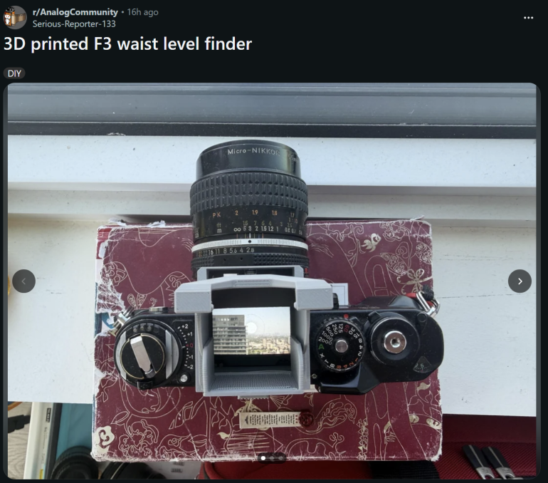 Top-down view of a camera with a 3D printed waist-level finder attached, placed on a red patterned surface.
