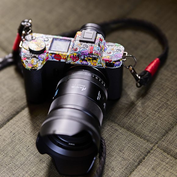 A camera with a colorful, sticker-covered body and a large lens rests on a textured, green surface.
