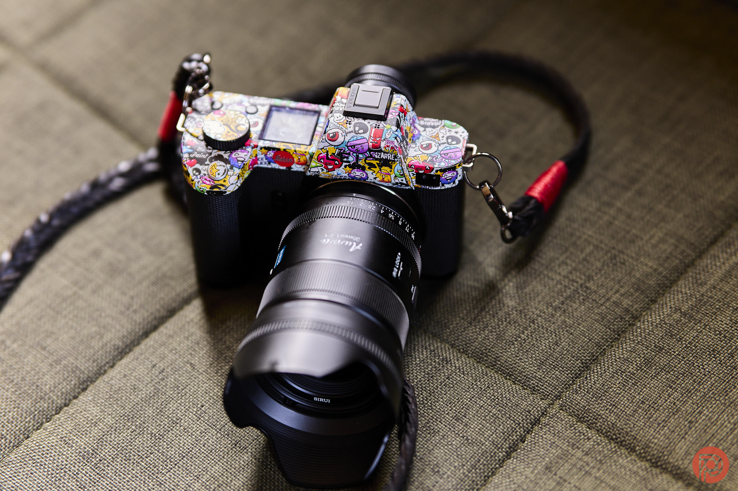 A camera with a colorful, sticker-covered body and a large lens rests on a textured, green surface.
