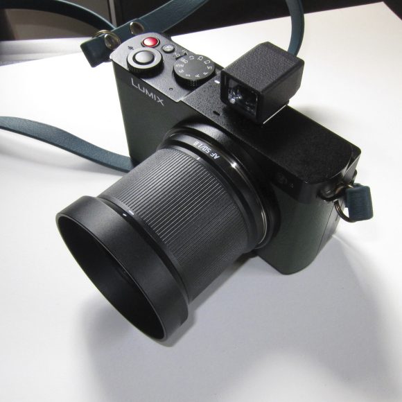 Black Lumix digital camera with large lens and blue strap resting on a white surface.
