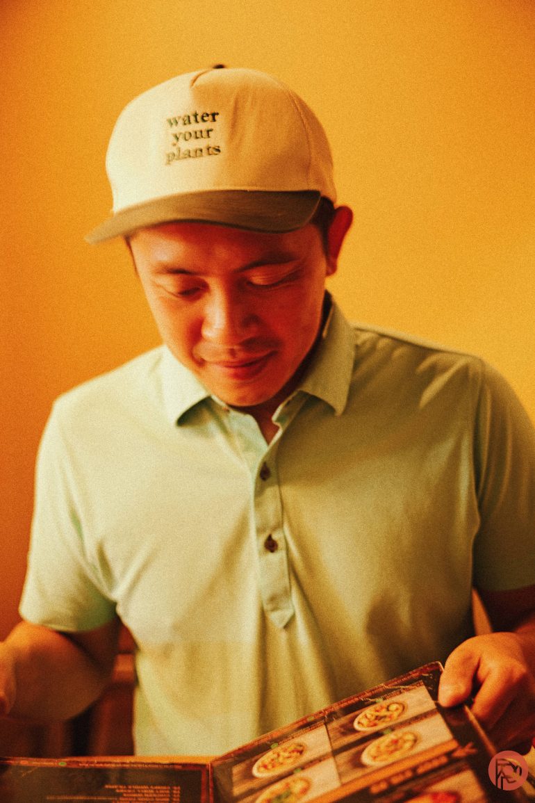 A man in a cap reading water your plants looks down at a menu in a warmly lit room.