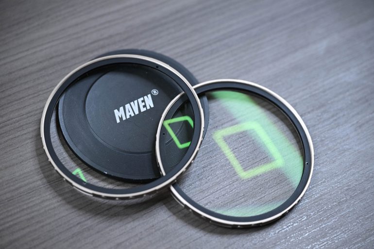 Two camera lens filters and a MAVEN lens cap on a wooden surface, with green reflections visible.
