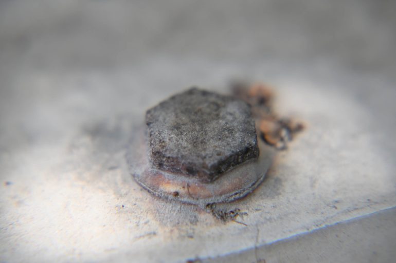 Close-up of a rusty, hexagonal bolt fastened to a weathered, light-colored metal surface.
