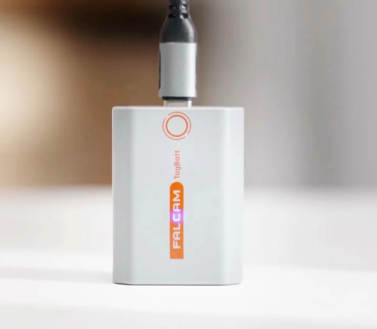 Small white FALCAM TagBot device with a cable plugged in, placed on a white surface.