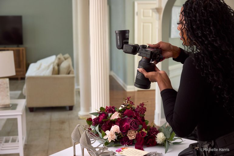 A woman photographs a bouquet and shoes on a table in a bright, elegant room.